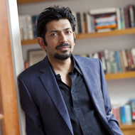 Siddhartha Mukherjee wearing a blue suit and standing in a library